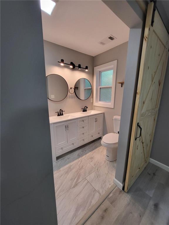 full bathroom with double vanity, toilet, visible vents, and a sink