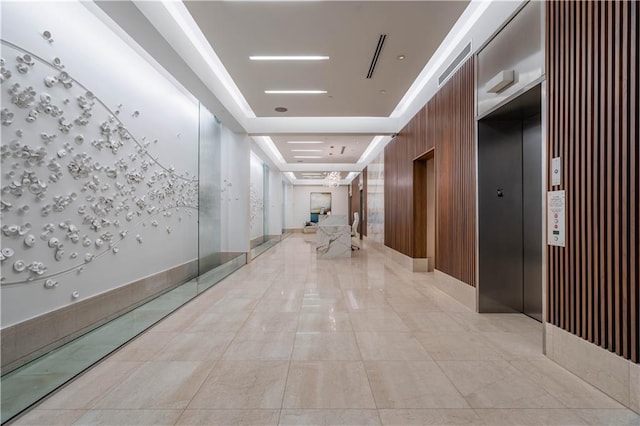 corridor featuring elevator, a tray ceiling, and light tile patterned floors