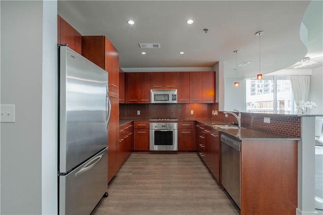 kitchen featuring sink, dark stone countertops, backsplash, stainless steel appliances, and decorative light fixtures