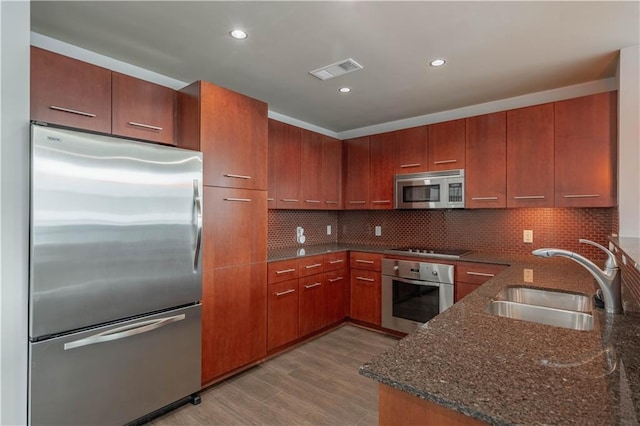 kitchen with sink, backsplash, stainless steel appliances, and dark stone counters