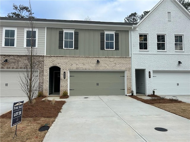 view of property featuring an attached garage, board and batten siding, concrete driveway, and brick siding