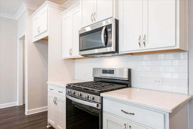 kitchen with dark wood-type flooring, ornamental molding, backsplash, white cabinetry, and appliances with stainless steel finishes