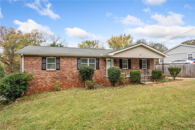 single story home featuring covered porch, fence, a front lawn, and brick siding