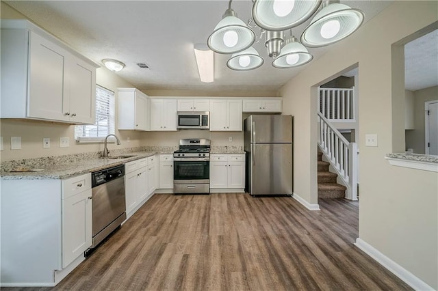 kitchen with hardwood / wood-style floors, white cabinetry, sink, decorative light fixtures, and stainless steel appliances