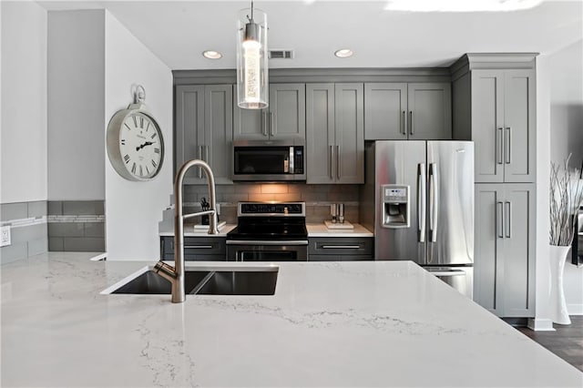 kitchen featuring appliances with stainless steel finishes, backsplash, light stone counters, sink, and gray cabinets