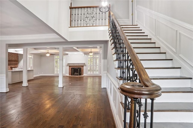 stairs featuring a decorative wall, a fireplace, wood finished floors, ornamental molding, and beam ceiling