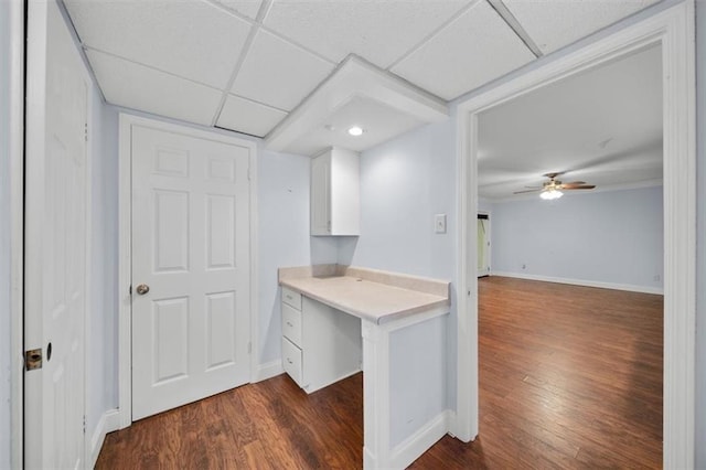 interior space featuring built in desk, ceiling fan, white cabinetry, a paneled ceiling, and dark hardwood / wood-style floors