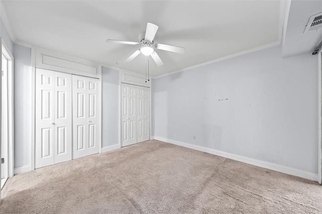 unfurnished bedroom featuring multiple closets, crown molding, carpet floors, and ceiling fan