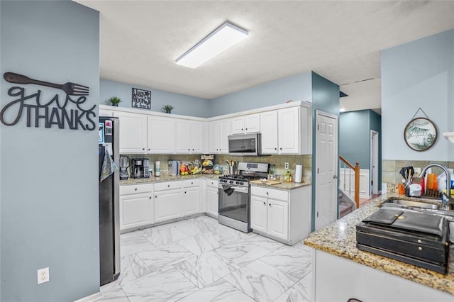 kitchen featuring marble finish floor, white cabinets, stainless steel appliances, and a sink