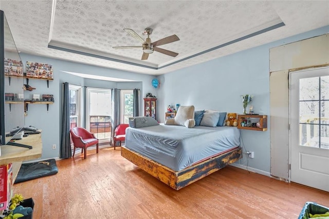 bedroom with a textured ceiling, a raised ceiling, and wood finished floors