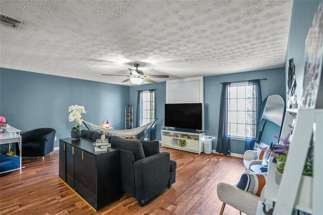 living area with visible vents, baseboards, a ceiling fan, and wood finished floors