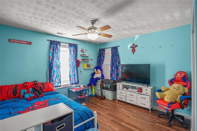 bedroom featuring visible vents, baseboards, wood finished floors, a textured ceiling, and a ceiling fan