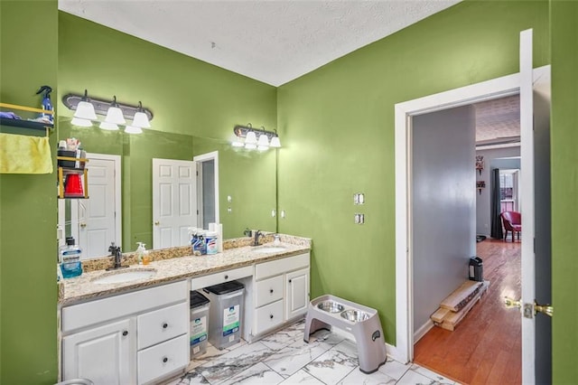 bathroom featuring double vanity, marble finish floor, a textured ceiling, and a sink