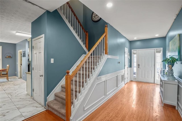 entryway with marble finish floor, recessed lighting, wainscoting, a decorative wall, and stairs