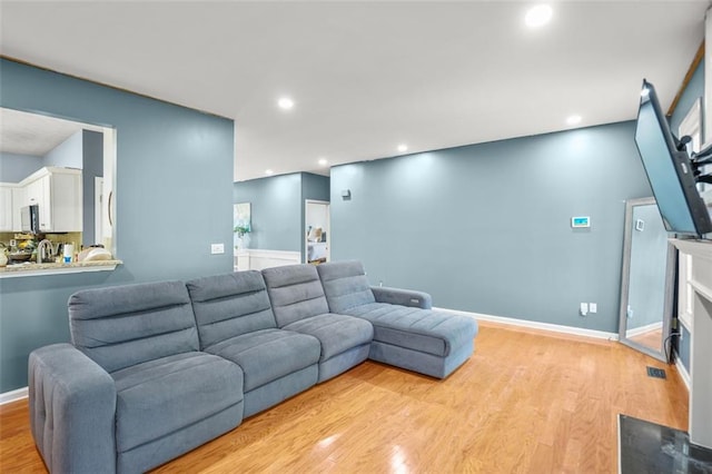 living area featuring a fireplace with flush hearth, recessed lighting, light wood-type flooring, and baseboards