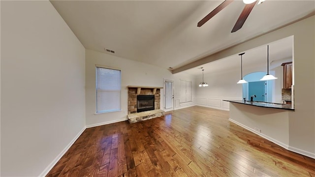 unfurnished living room featuring a stone fireplace, sink, beamed ceiling, hardwood / wood-style flooring, and ceiling fan with notable chandelier