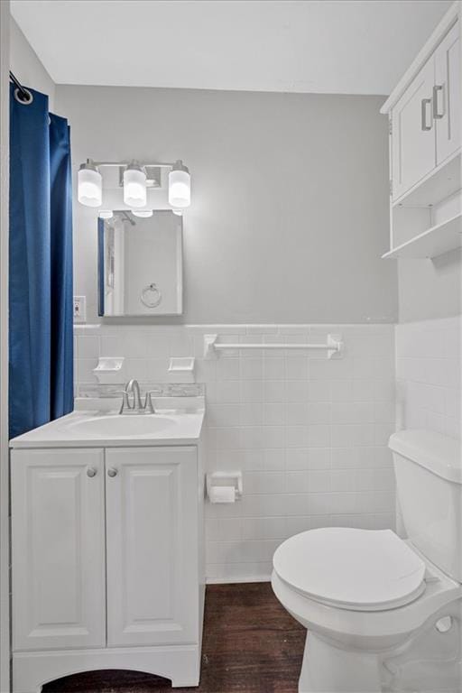 bathroom featuring vanity, toilet, a wainscoted wall, tile walls, and wood finished floors