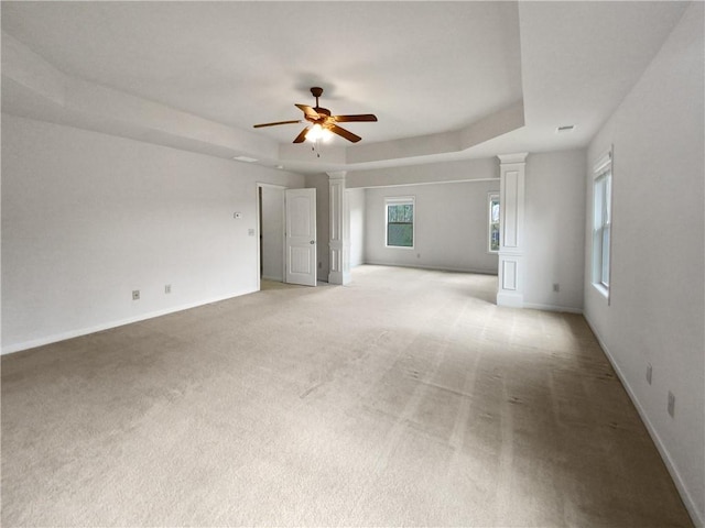 carpeted empty room with a tray ceiling, ceiling fan, and decorative columns