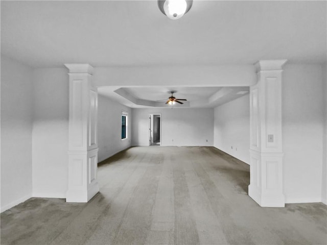 carpeted empty room featuring a tray ceiling, ceiling fan, and decorative columns