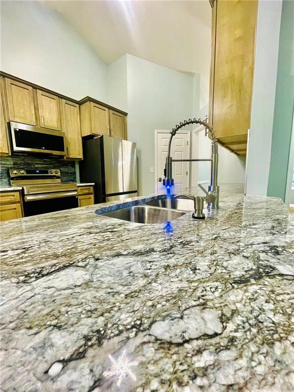 7675 Lanier View Rdg, Cumming, GA 30041 - kitchen with appliances with stainless steel finishes, light stone counters, a sink, backsplash, and vaulted ceiling