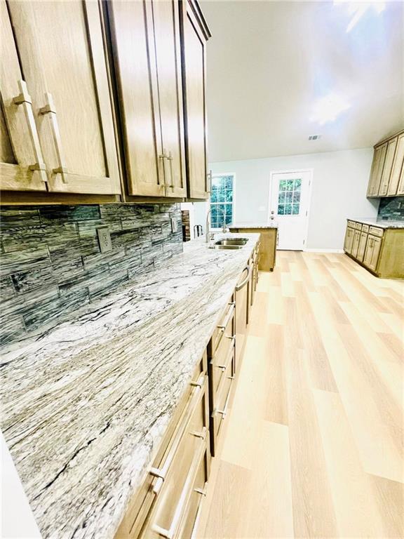 7675 Lanier View Rdg, Cumming, GA 30041 - kitchen featuring a sink, backsplash, light wood-type flooring, light stone countertops, and baseboards