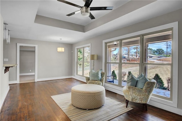 sitting room with a tray ceiling, ceiling fan, baseboards, and wood finished floors