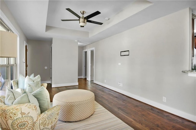 living room with dark wood-style floors, baseboards, a raised ceiling, and a ceiling fan