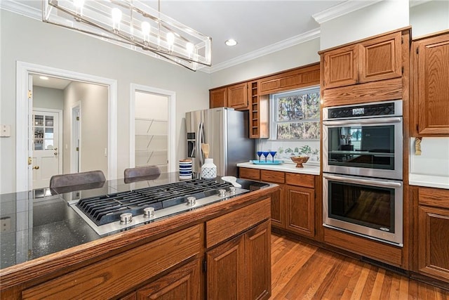 kitchen with appliances with stainless steel finishes, brown cabinets, wood finished floors, crown molding, and pendant lighting