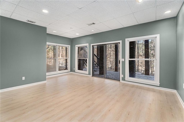 empty room with a drop ceiling, wood finished floors, visible vents, and baseboards