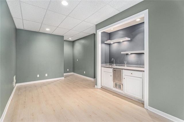 bar featuring indoor wet bar, light wood-style flooring, baseboards, and a drop ceiling