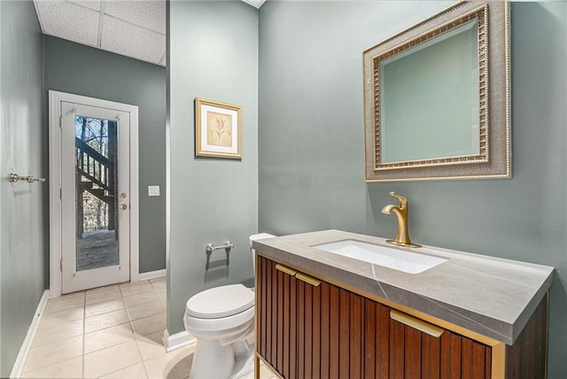 bathroom featuring a paneled ceiling, toilet, vanity, tile patterned flooring, and baseboards