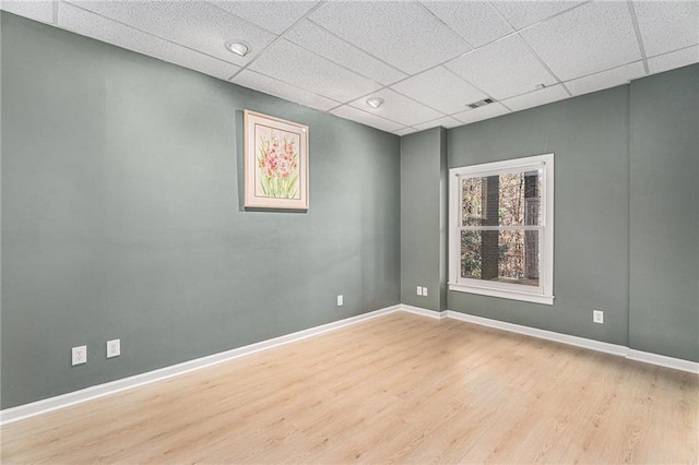 empty room with visible vents, wood finished floors, a paneled ceiling, and baseboards