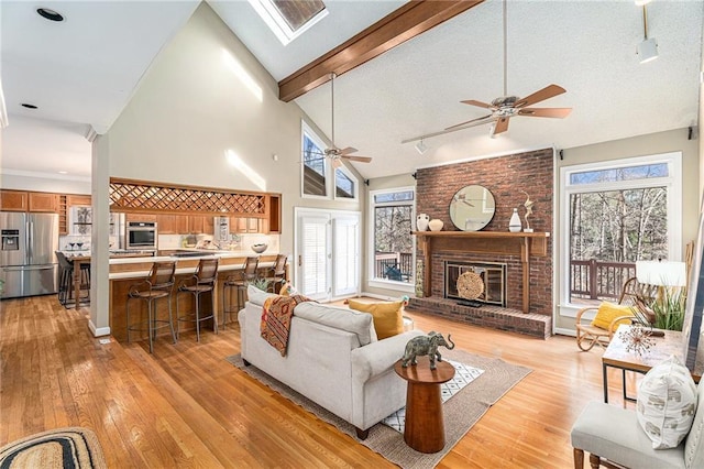 living room with high vaulted ceiling, a fireplace, beam ceiling, light wood finished floors, and rail lighting