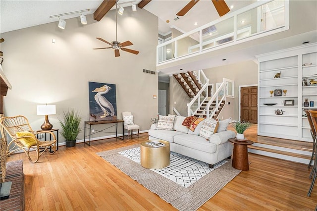 living area with ceiling fan, high vaulted ceiling, wood finished floors, baseboards, and stairs