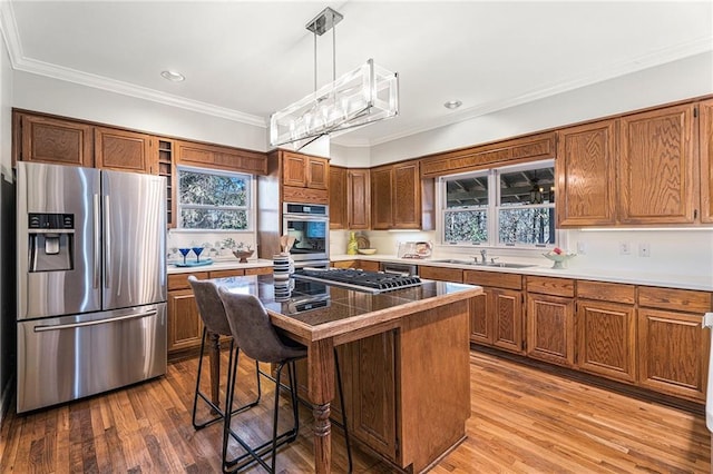 kitchen with a breakfast bar, wood finished floors, a sink, appliances with stainless steel finishes, and brown cabinets