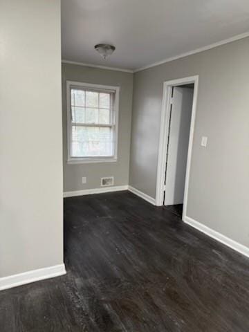 empty room with dark wood finished floors, crown molding, and baseboards