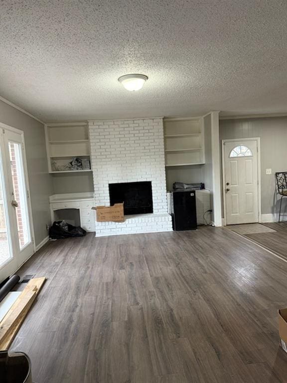 unfurnished living room with a textured ceiling, a brick fireplace, wood finished floors, and baseboards