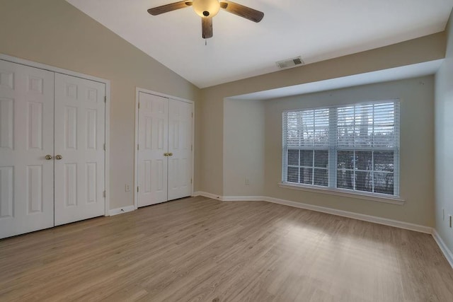 unfurnished bedroom featuring light wood-type flooring, ceiling fan, vaulted ceiling, and two closets