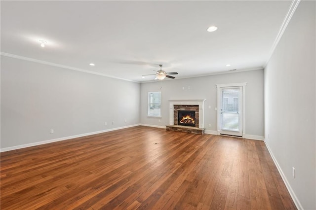 unfurnished living room featuring ceiling fan, crown molding, hardwood / wood-style flooring, and a stone fireplace