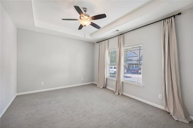 carpeted spare room featuring a tray ceiling and ceiling fan