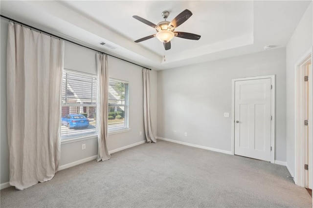 unfurnished room with ceiling fan, a raised ceiling, and light colored carpet