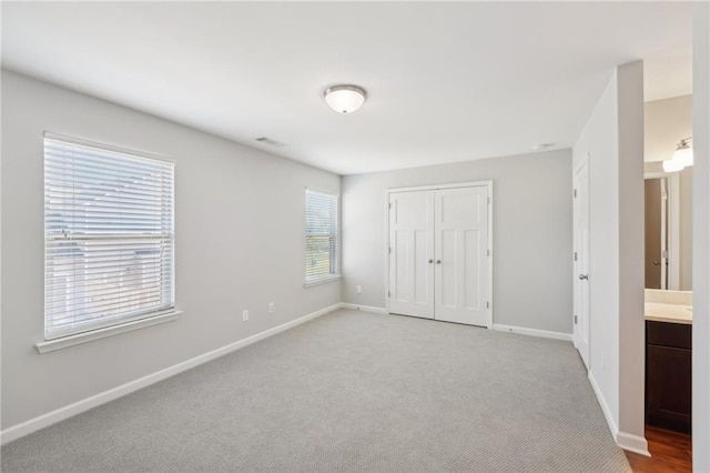 unfurnished bedroom featuring a closet, ensuite bathroom, and light carpet