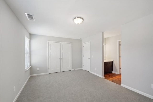 unfurnished bedroom featuring connected bathroom, light carpet, and a closet