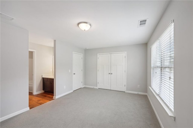 unfurnished bedroom featuring light colored carpet, a closet, and ensuite bath