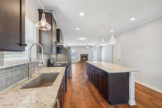 kitchen with tasteful backsplash, sink, black range oven, decorative light fixtures, and light stone counters