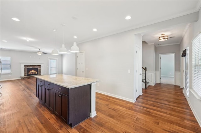 kitchen with a kitchen island, a stone fireplace, dark brown cabinetry, decorative light fixtures, and crown molding