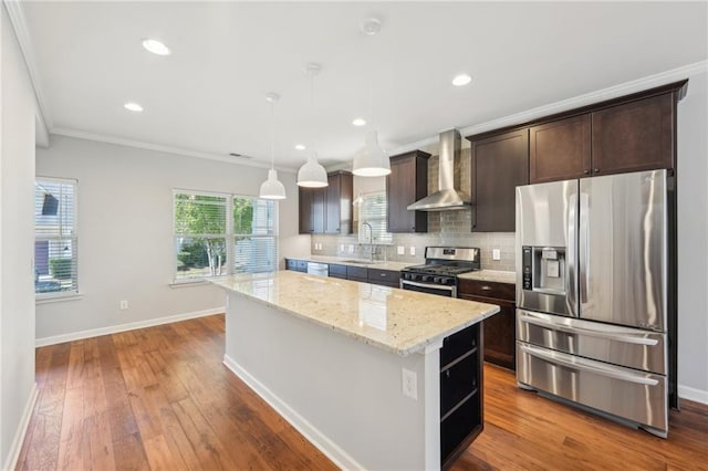 kitchen featuring wall chimney range hood, sink, a center island, stainless steel appliances, and pendant lighting