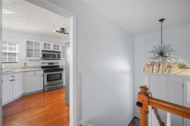 kitchen featuring appliances with stainless steel finishes, white cabinetry, glass insert cabinets, and an inviting chandelier