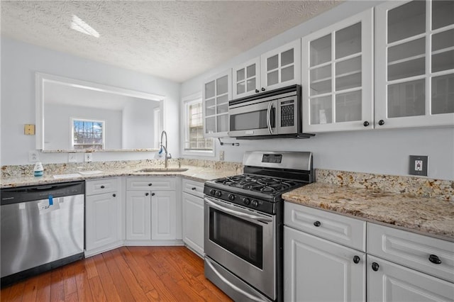 kitchen featuring stainless steel appliances, glass insert cabinets, a sink, and white cabinetry