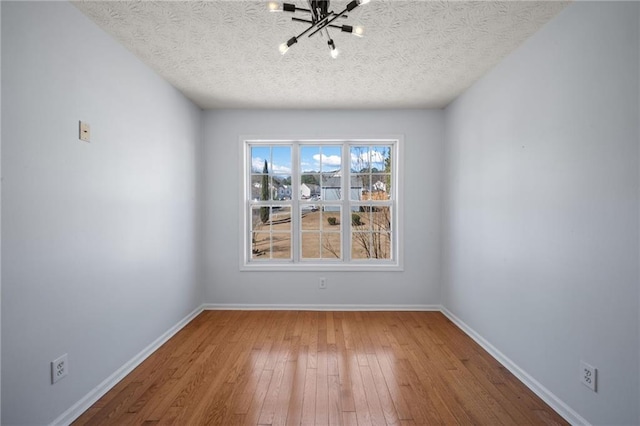 spare room featuring a textured ceiling, baseboards, and hardwood / wood-style floors